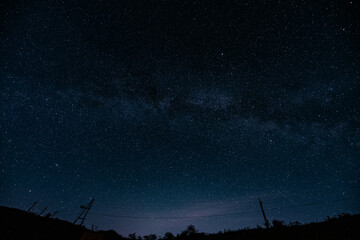 Night starry sky and hills with power lines. Milky way background