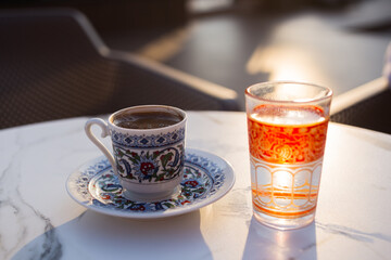 Turkish coffee in a cup with national ornament and a cup of water on a table on the street in a cafe. Sunset sun