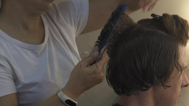 Assian hairdresser's hands hold pieces. Master makes haircut with scissors. Client is sitting in chair. High quality 4k footage