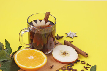 mulled wine in glass mug with spices on yellow background