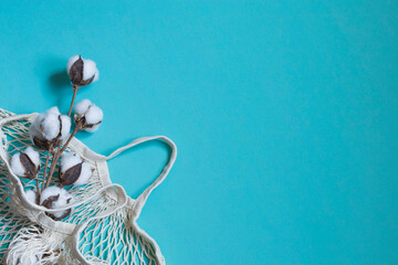 Cotton flowers on a branch on a pastel blue background. Composition for the holiday of flowers. Shopping bag made from natural ecological raw materials. Flat lay, top view, copy space.