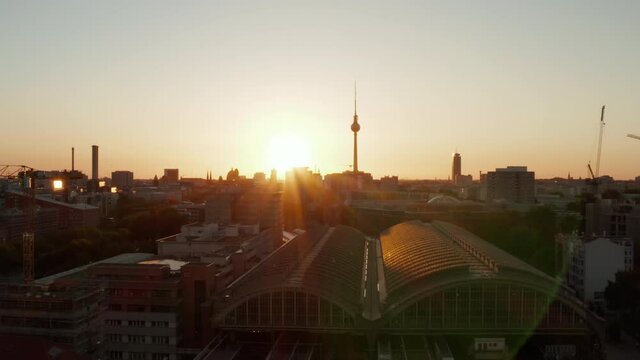 AERIAL: Flight over Berlin, Germany Ostbahnhof Central Train Station at beautiful Sunset, Sunlight and view on Alexanderplatz TV Tower, Sunflairs
