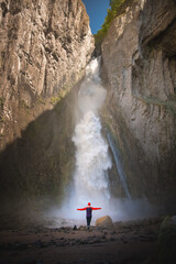 A full-length portrait of a young adult woman stands in front of a waterfall. The idea of a healthy...