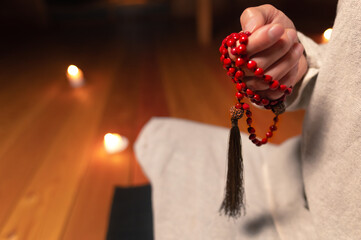 close-up the male hand of a monk practicing meditation holds a red rosary in a dark room by...