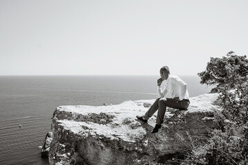 Fototapeta premium A pensive young man sits at a cliff. Portrait of a guy by the sea.