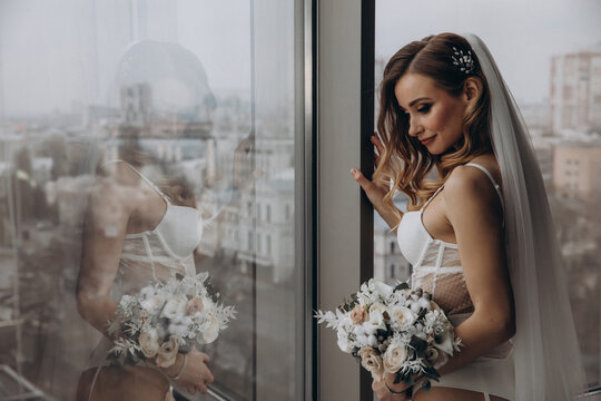 Bride with a wedding bouquet. Morning girl in a peignoir. Glamorous photo session by the window.