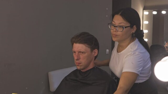 Assian master hairdresser frees caucasian client from rest of his hair after haircut. Haircut in salon. Make up for filming. High quality 4k footage