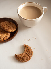 Oatmeal cookies in a wooden plate and a cup of coffee with milk on a white background
