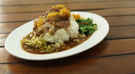 A stewed pork leg on rice with a a yellow sauce recipe on top on the wood table.
