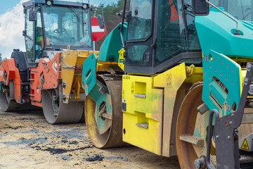 Fototapeta premium Asphalt paver machine and steam road roller during road construction and repairing works, process of asphalting and paving, workers working on the new road construction site