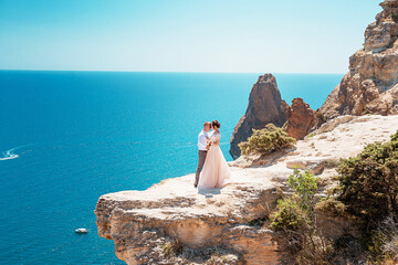The groom and the bride stand on a cliff, and against the background of a beautiful sea