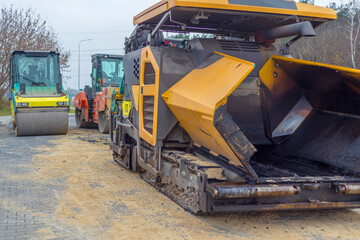 Asphalt paver machine and steam road roller during road construction and repairing works, process of asphalting and paving, workers working on the new road construction site