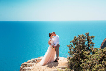 The groom and the bride stand on a cliff, and against the background of a beautiful sea