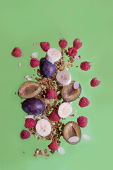 Flying granola, raspberry, plum, banana, almond petals, cedar nuts on a green background. Food levitation. Vertical orientation