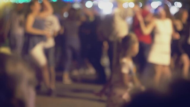 Many couples are dancing social dances in the street and there is little funny girl on foreground trying to imitate, defocused real-time shot.