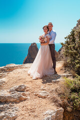 Fototapeta na wymiar The groom and the bride stand on a cliff, and against the background of a beautiful sea