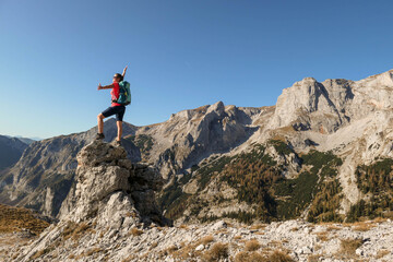 Fototapeta premium Woman standing on top of a sharp, pointy boulder in Hochschwab region, Austrian Alps. The steep mountain wall in front look very dangerous. High mountaineering. Autumn vibes. Adventure and freedom