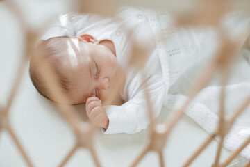Adorable baby in a white sunny bedroom. Newborn baby is resting in bed. Family morning at home.