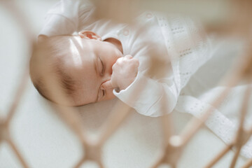 Adorable baby in a white sunny bedroom. Newborn baby is resting in bed. Family morning at home.