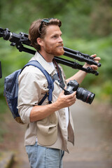 man in a forest holding a dslr camera and tripod