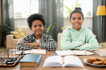 Happy elementary girl and boy in casualwear sitting by table in living-room