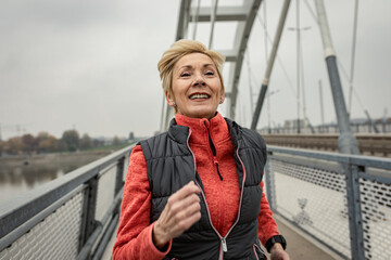 Active senior woman running through the city during the day.