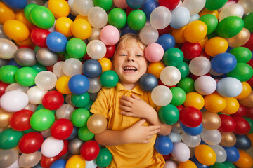 Fototapeta na wymiar Portrait of happy child laughing while lying in pool among colored balls