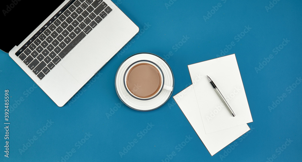 Wall mural Top view of a cup of coffee, laptop, papers, and a pen on a blue surface