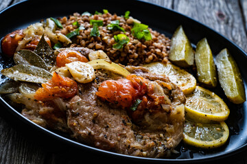 Roasted meat, buckwheat and pickled cucumbers lemon and toamtoes on wooden table
