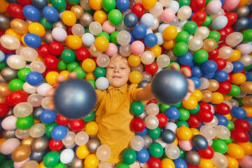 Fototapeta na wymiar Portrait of happy child lying among colored balls and throwing the balls up