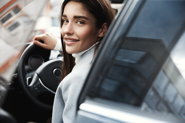 Close-up of elegant businesswoman open car door and smiling at camera. Female entrepreneur driving...