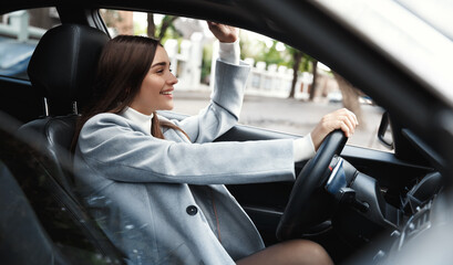 Business. Happy busiensswoman driving car and waving hand at friend. Elegant female driver heading...
