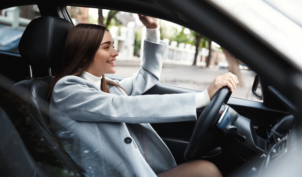 Business. Happy busiensswoman driving car and waving hand at friend. Elegant female driver heading on meeting, saying hello