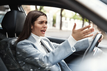 Annoyed businesswoman stuck in traffic on her commute. Angry female executive complaining while driving car, scolding another driver