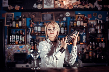Experienced girl barman is pouring a drink while standing near the bar counter in pub