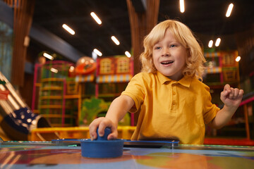 Fototapeta na wymiar Little boy with blond hair playing table hockey in the amusement park