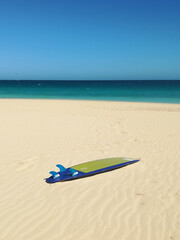 Fototapeta na wymiar Yellow and blue surfboard resting on the sand