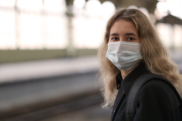 girl at the train station wearing a medical mask