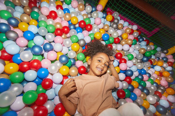 Fototapeta na wymiar Portrait of African happy little girl lying among colored balls in dry pool