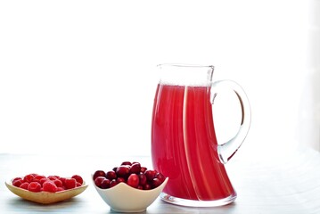 ripe raspberries and cranberries, a drink in a decanter and a glass on a wooden table