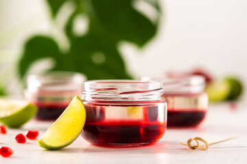 Red alcoholic shots on white background , small jars with liquor and grenadine with lime