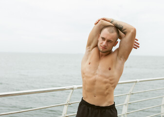 Muscular man with a naked torso doing hand stretch before training on the beach