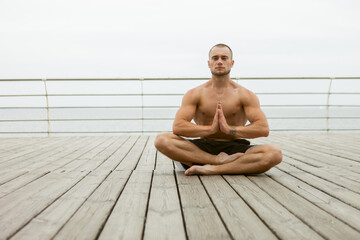 Fototapeta na wymiar Muscular athlete man with a naked torso meditates on the beach. Practicing yoga hatha