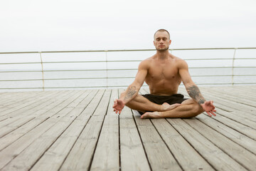 Muscular athlete man with a naked torso meditates on the beach. Practicing yoga hatha