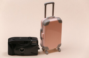 Travel or trip concept. Mini plastic travel suitcase and camera on beige background. Minimal style