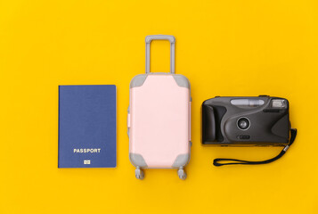 Travel flat lay. Mini plastic travel suitcase, camera and passport on yellow background. Minimal style. Top view
