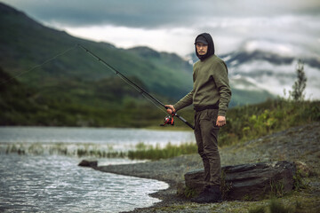 Man fishing with spinning on the bank of scenic mountain lake