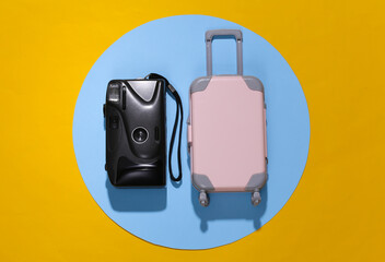 Travel minimalism. Mini plastic travel suitcase and camera on yellow blue background with deep shadow. Minimal style. Top view, flat lay
