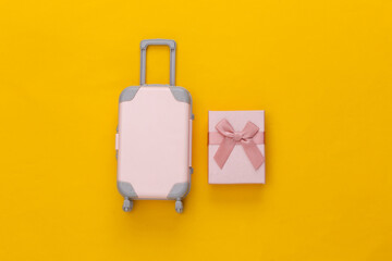 Travel concept. Mini plastic travel suitcase and gift box on yellow background. Minimal style. Top view, flat lay