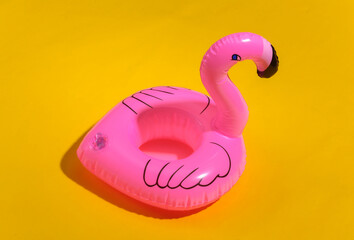 Inflatable pink flamingo on yellow sunny background. Summer vacation concept.